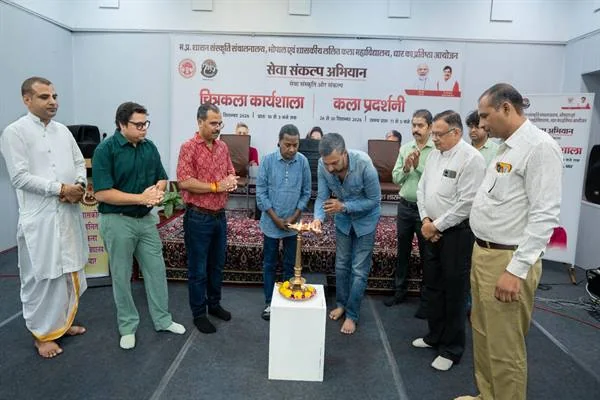 चित्रकला कार्यशाला के शुभारंभ पर दीप प्रज्वलित करते लोग, आसपास खड़े अतिथि और पीछे कार्यक्रम का बैनर