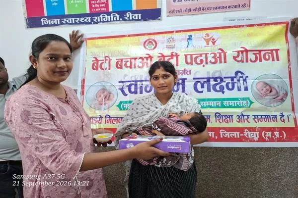 अस्पताल में एक महिला नवजात बच्ची को गोद में लिए हुए है और दूसरी महिला उसे स्वच्छता किट भेंट कर रही है; पीछे ‘बेटी बचाओ बेटी पढ़ाओ’ का बैनर लगा है।