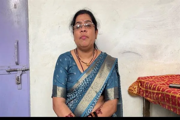 नीली साड़ी पहने चश्माधारी महिला कमरे में कुर्सी पर बैठी हुई