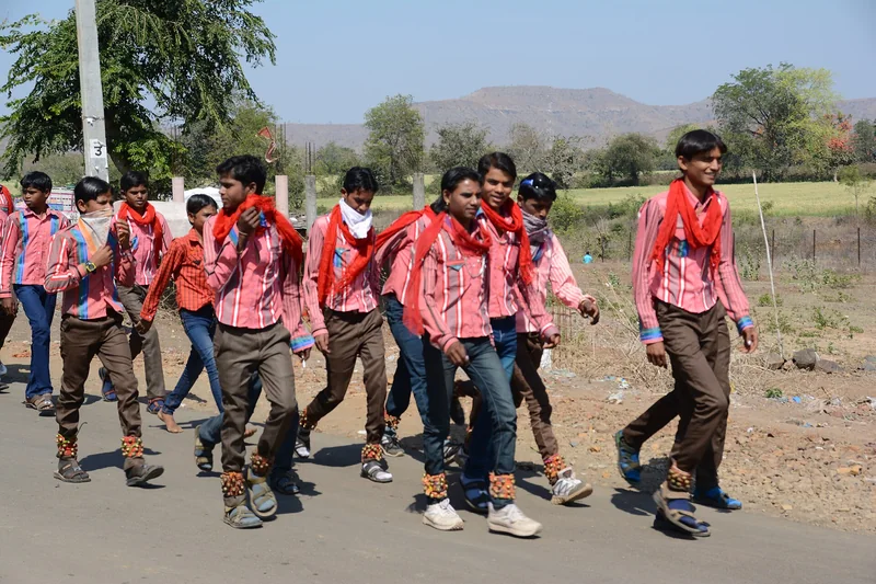खेत की मेड़ पर खड़े महिला-पुरुषों का समूह, पीछे बड़ा पेड़ और नदी दिखाई दे रही है।